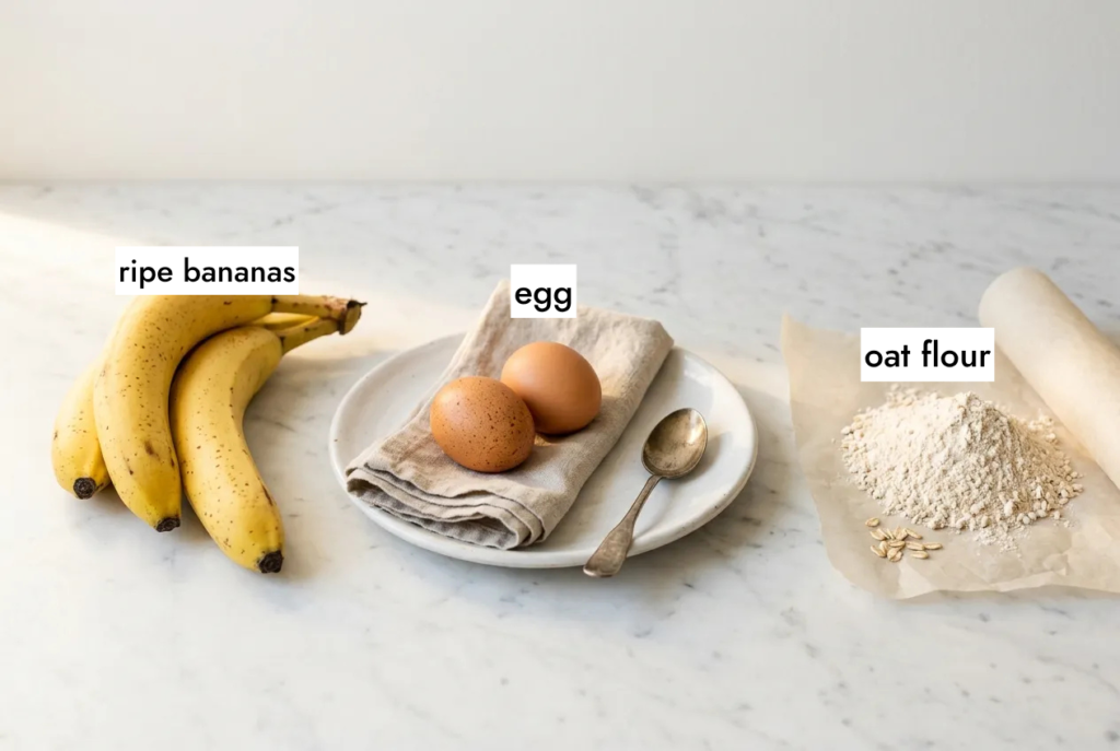 3 ingredient banana bread ingredients flat lay — ripe bananas, eggs and oat flour on white marble countertop