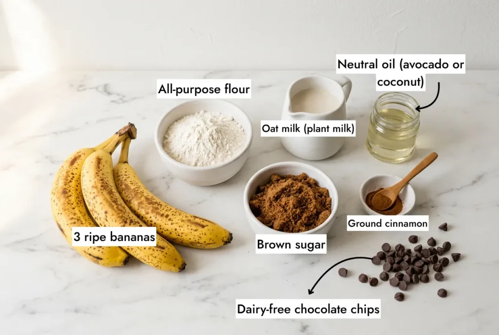 Vegan banana bread ingredients flat lay — ripe bananas, flour, brown sugar, oat milk, oil, cinnamon on white marble