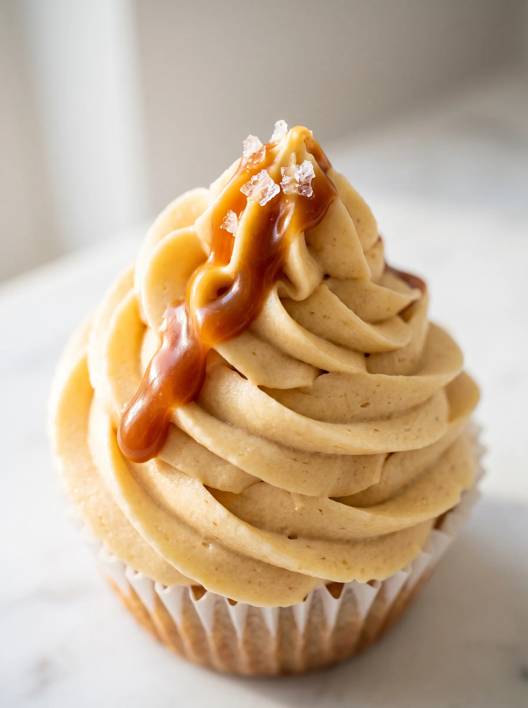 Close-up of banana cupcake with salted caramel drizzle on swirled buttercream frosting and flaky sea salt