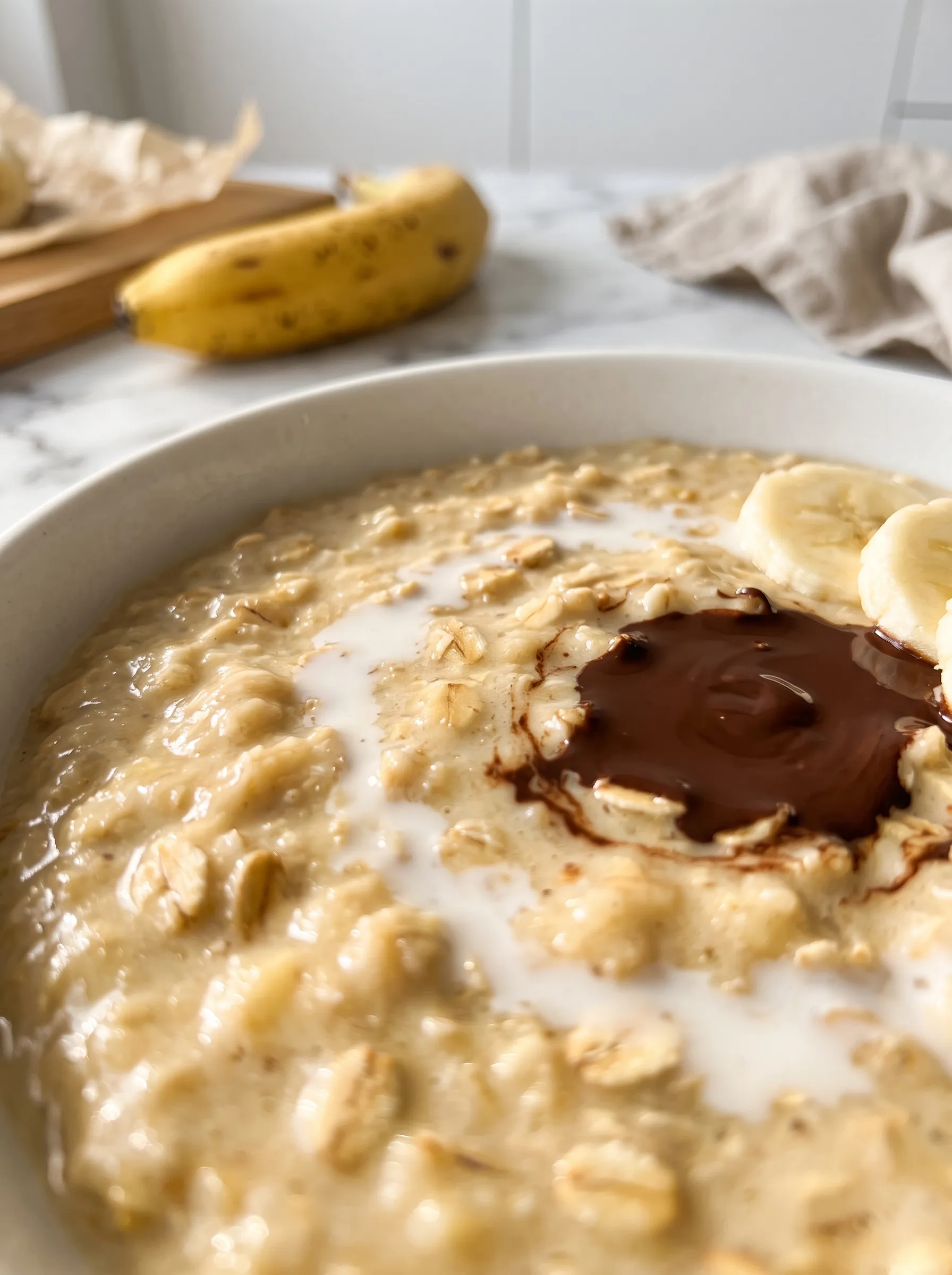 Close-up of creamy banana oatmeal texture with a pool of melted chocolate and a swirl of milk