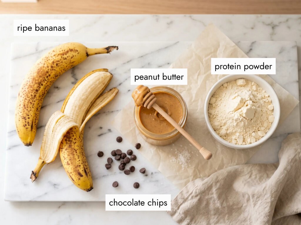 3 ingredients for peanut butter banana protein cookies — ripe bananas, creamy peanut butter, and vanilla protein powder on white marble