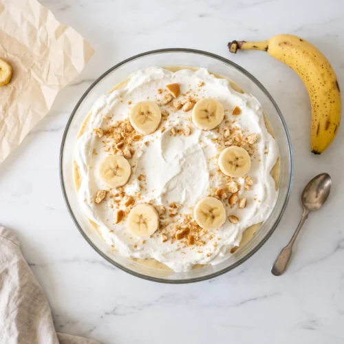 overhead view of classic banana pudding recipe in a glass trifle dish — showing creamy top layer with crushed nilla wafers and banana slices, vanilla wafer banana pudding
