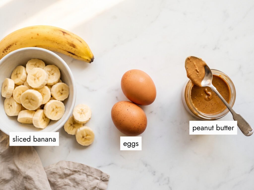 3 ingredients flourless peanut butter banana pancakes sliced banana in white bowl two brown eggs natural peanut butter white marble flat lay
