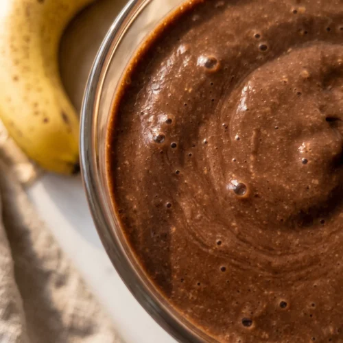 Banana chocolate smoothie recipe in a clear glass, thick and topped with dark chocolate shards