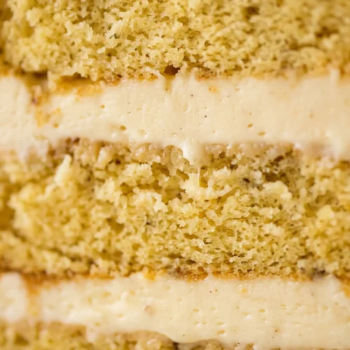Extreme close-up of banana cream layer cake cross-section showing thick ivory pastry cream and soft golden banana cake texture