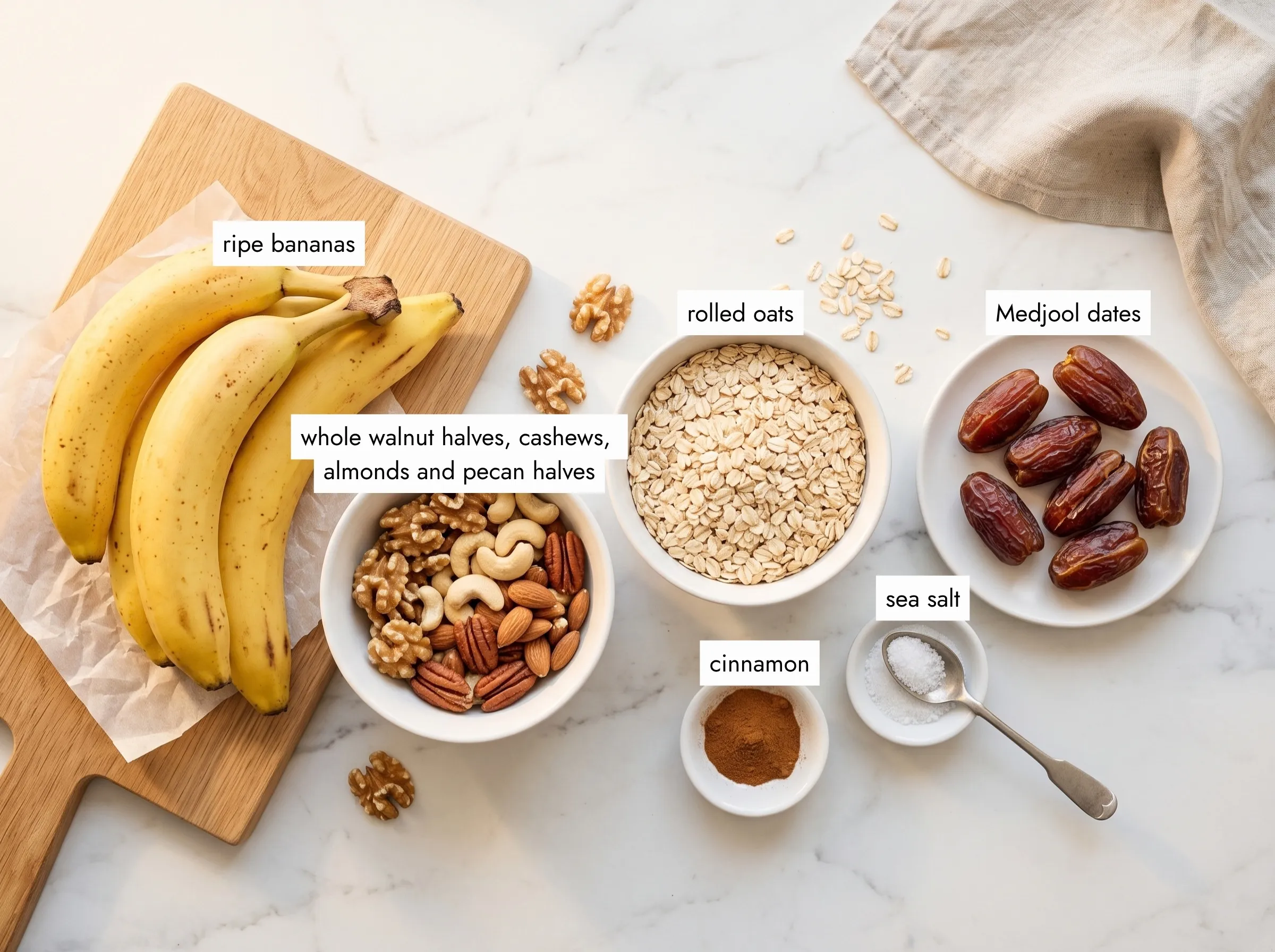 Banana granola bars ingredients: ripe bananas, Medjool dates, mixed nuts, rolled oats, cinnamon and sea salt on marble