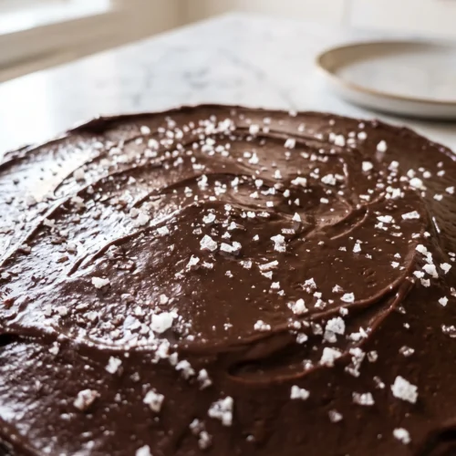 Close-up of glossy set chocolate fudge frosting on banana cake with fleur de sel crystals catching morning light